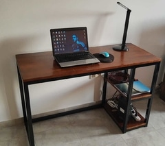 Escritorio moderno de madera oscura con estructura de metal negro, tiene dos estantes laterales. Sobre él hay una lámpara, un ordenador portátil y un mouse. Ideal para trabajo o estudio.