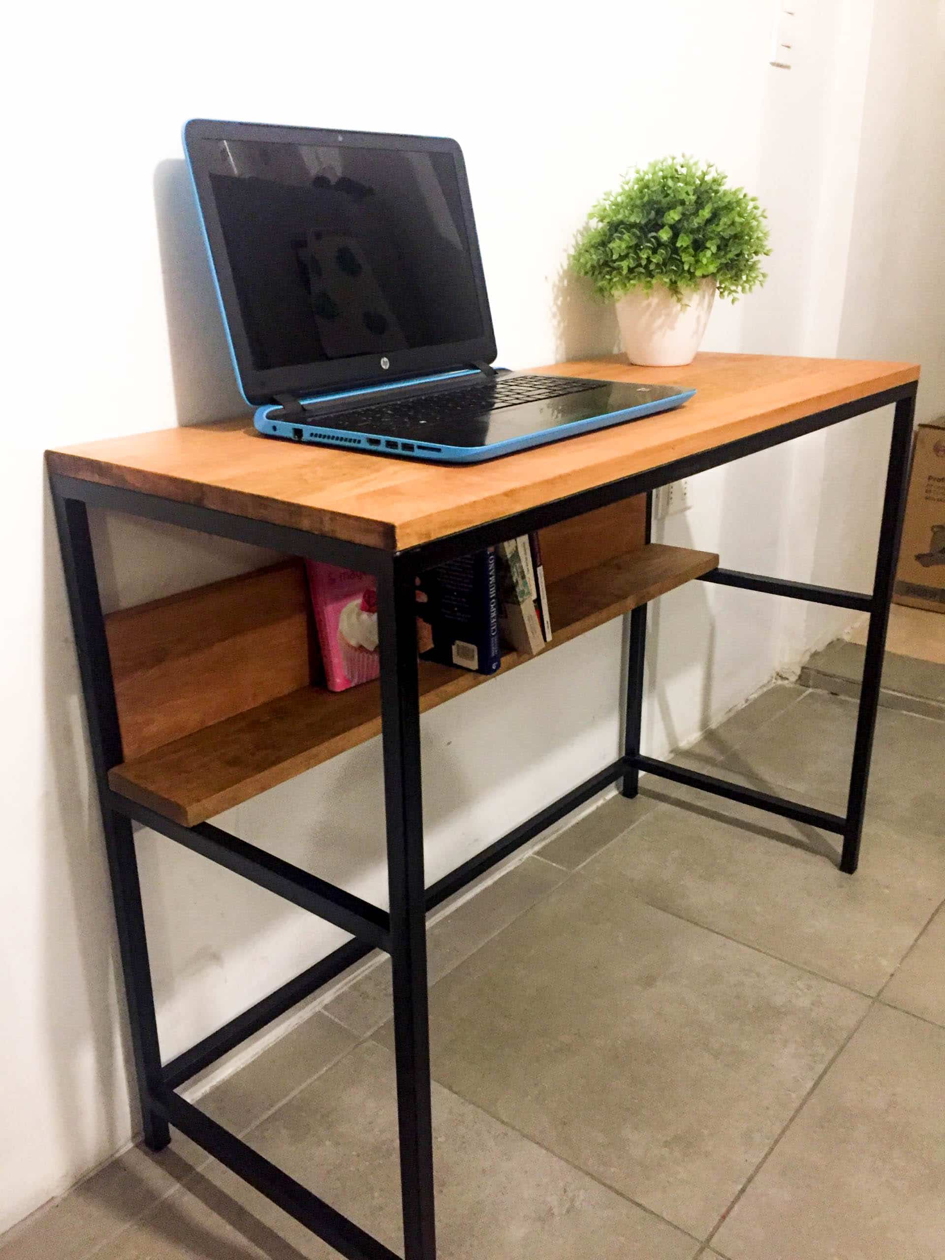 Escritorio de madera con estructura metálica negra, estante inferior integrado y superficie despejada, ideal para oficinas modernas o espacios de estudio compactos.