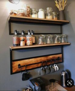 Estantería de pared de madera con soporte metálico negro, dos niveles para frascos y botellas, barra inferior con ganchos para tazas. Ideal para almacenamiento de cocina.