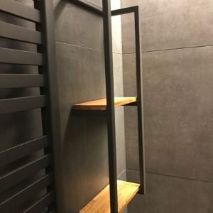 Estantería moderna de baño con estructura metálica negra y dos baldas de madera, montada sobre pared de azulejos grises. Diseño minimalista y funcional.
