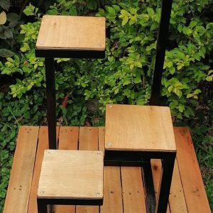 Estante de madera y metal negro con diseño escalonado, ideal para macetas o decoración, colocado sobre una plataforma de madera al aire libre.