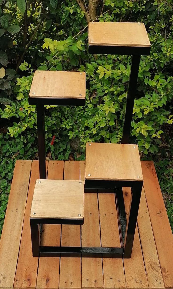 Estante de madera y metal negro con diseño escalonado, ideal para macetas o decoración, colocado sobre una plataforma de madera al aire libre.