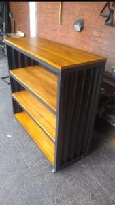 Estante de metal y madera con cuatro repisas. Diseño industrial, estructura negra y superficie de madera clara, ideal para almacenar o exhibir objetos en interiores.