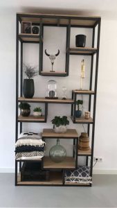 Estantería alta de madera con marco metal negro, múltiples estantes decorados con plantas, libros y objetos diversos, ideal para salas modernas.