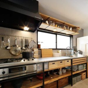 Cocina moderna con encimera de acero inoxidable, estantes abiertos de madera y estructura de metal negro. Cajones y espacio de almacenamiento inferior con cajas organizadoras.