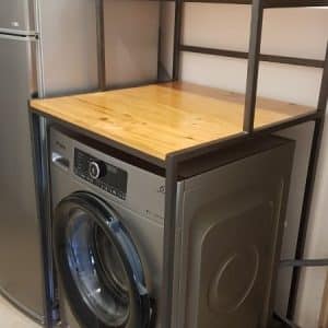 Mueble de metal con encimera de madera, diseñado para integrar una lavadora. Incluye un estante superior para dispositivos como microondas. Ideal para optimizar espacio en áreas de lavado.