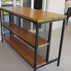 Mesa de diseño industrial con estructura de metal negro y estantes de madera. Cuenta con tres niveles y laterales de rejilla metálica. Ideal para espacios modernos o lofts.