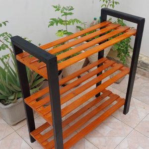 Estante de madera, color naranja con marco negro, de tres niveles, estilo moderno y minimalista. Ideal para plantas o almacenamiento, ubicado en un espacio exterior pavimentado.