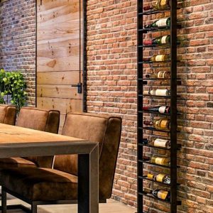 Estante de metal vertical para botellas de vino, montado en una pared de ladrillo. Diseño elegante y moderno, ideal para almacenamiento decorativo en interiores contemporáneos.