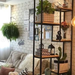 Estantería metálica negra con estantes de madera, decorada con plantas y adornos, contra una pared de ladrillo blanco.