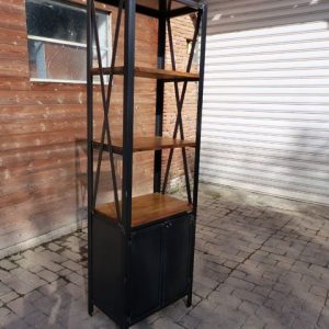 Estantería estrecha de metal y madera con estructura negra y cuatro niveles de almacenaje, incluyendo un armario inferior con puertas. Diseño industrial y moderno para espacios reducidos.