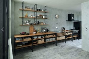 Cocina minimalista con estantes de madera y marco de metal negro. Muebles abiertos con cajones y cestas, integrados con una encimera amplia. Diseño funcional y moderno.