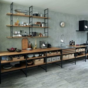 Cocina minimalista con estantes de madera y marco de metal negro. Muebles abiertos con cajones y cestas, integrados con una encimera amplia. Diseño funcional y moderno.