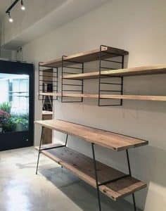 Estantería de madera con estructura metálica negra, incluye varios estantes rectangulares montados en la pared y un escritorio a juego con patas inclinadas, estilo industrial.