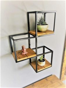 Estantería de pared moderna con marco de metal negro y estantes de madera en forma de cubos, utilizada para decorar con plantas y figuras pequeñas.