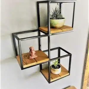 Estantería de pared moderna con marco de metal negro y estantes de madera en forma de cubos, utilizada para decorar con plantas y figuras pequeñas.