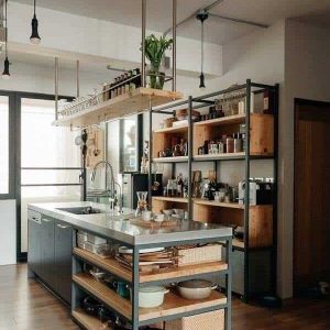 Isla de cocina moderna con estantes abiertos, encimera metálica y espacio de almacenamiento para utensilios. Estantes de madera oscura organizan accesorios en un ambiente contemporáneo.