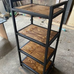 Estante de metal negro con cuatro repisas de madera oscura, ideal para almacenamiento en interiores; diseño rústico y funcional en taller o estudio.