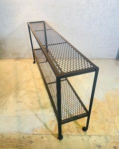 Estantería de metal de estilo industrial con diseño de rejilla, dos niveles y estructura rectangular negra, ideal para espacios modernos.