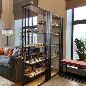 Estantería moderna de metal negro y madera clara, con múltiples repisas, perfecta para exhibir colecciones en una sala de estar elegante y contemporánea.