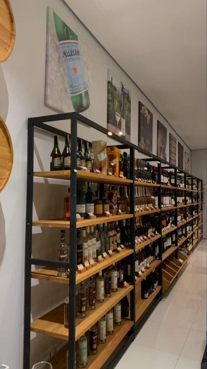 Estantería de metal con repisas de madera, repleta de botellas de vino y licor, alineada a lo largo de la pared en una tienda especializada.