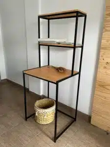 Estantería alta de metal negro con estantes de madera clara. Cuenta con dos niveles superiores y una mesa de trabajo. Ideal para organizar y decorar espacios interiores.