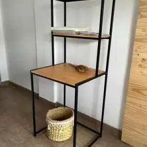 Estantería alta de metal negro con estantes de madera clara. Cuenta con dos niveles superiores y una mesa de trabajo. Ideal para organizar y decorar espacios interiores.