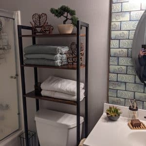 Estantería de baño de metal con tres niveles, decorada con toallas, maceta de bonsái y adornos en forma de corazón. Elegante y funcional, optimiza el espacio sobre el inodoro.