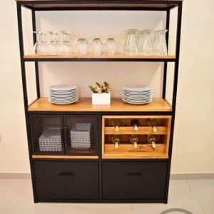 Estantería de metal y madera con tres niveles: cristalería, platos, puerta de rejilla y espacio para botellas, además de dos cajones inferiores para almacenamiento.