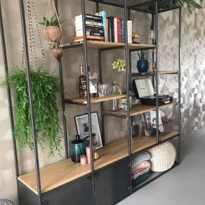 Estantería moderna con estructura metálica negra y estantes de madera. Incluye varias plantas, libros y objetos decorativos en un ambiente contemporáneo.