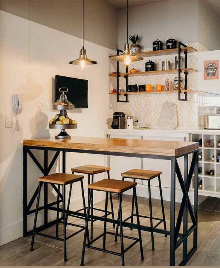 Mesa alta de madera clara con base de metal negro en diseño industrial, acompañada de cuatro taburetes a juego, en un espacio de cocina moderno y minimalista.