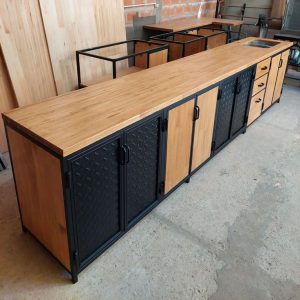 Gabinete industrial largo con superficie de madera clara. Tiene puertas en negro con relieve, tiradores de metal y laterales de madera. Ideal para talleres o cocinas modernas.