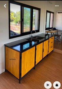 Gabinete de cocina con superficie negra brillante, cuerpo de madera clara y estructura metálica negra, que integra un fregadero en un diseño moderno y funcional.