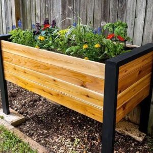 Jardinera elevada de madera con acabado natural y estructura de patas negras, utilizada para plantar flores coloridas. Ideal para jardines de exterior, aportando un diseño moderno y funcional.