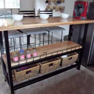 Isla de cocina de madera y metal con dos estantes. En el inferior, canastas de mimbre; en el superior, frascos de especias. Diseño funcional y moderno para almacenamiento.