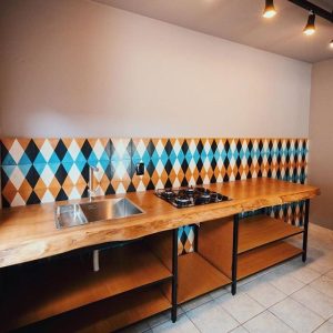 Encimera de madera con estufa empotrada y fregadero de acero inoxidable, sobre estantes abiertos de madera y metal en una cocina.