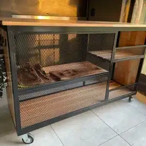 Mesa de trabajo industrial con estructura de metal negro, estantes de madera y paneles de malla. Montada sobre ruedas para facilitar su movilidad, ideal para espacios de cocina o taller.