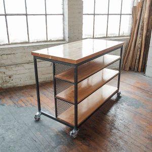 Isla de cocina industrial con estructura metálica negra, estantes de madera y ruedas. Encimera espaciosa y diseño funcional para espacios de trabajo versátiles y modernos.