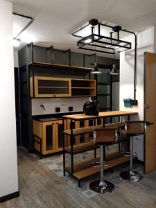 Mueble de cocina con estilo industrial, estantes abiertos en madera clara y metal negro, barra integrada y taburetes de metal cromado con asientos de madera.