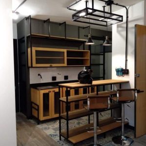 Mueble de cocina con estilo industrial, estantes abiertos en madera clara y metal negro, barra integrada y taburetes de metal cromado con asientos de madera.