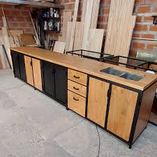 Gabinete de cocina rústico con encimera de madera y fregadero integrado. Posee puertas y cajones en tonos madera y negro, ideal para un taller o cocina industrial.