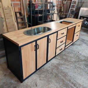 Gabinete de cocina de madera clara con marco negro, fregadero de acero inoxidable, tres puertas, cuatro cajones y espacio abierto para electrodomésticos.