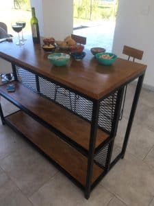 Mesa alta de madera con estructura metálica negra, dos estantes de rejilla y diseño moderno. Ideal para espacio de comedor o cocina.