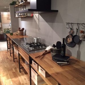 Cocina moderna con encimeras de madera clara, estanterías abiertas, campana extractora negra y estufa de gas integrada, ofrece un diseño elegante y funcional.