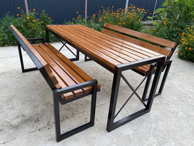 Juego de mesa y bancos de exterior con estructura de metal negro y superficies de madera pulida. Diseño moderno y resistente, ideal para jardines o terrazas.