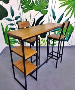 Mesa alta de madera con estructura de metal negro, acompañada de dos sillas a juego. Diseño moderno e industrial, adecuada para cocinas o bares pequeños.