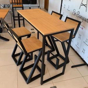 Conjunto de comedor moderno con estructura metálica negra y superficies de madera clara. Incluye mesa alta rectangular y sillas a juego con diseño geométrico.