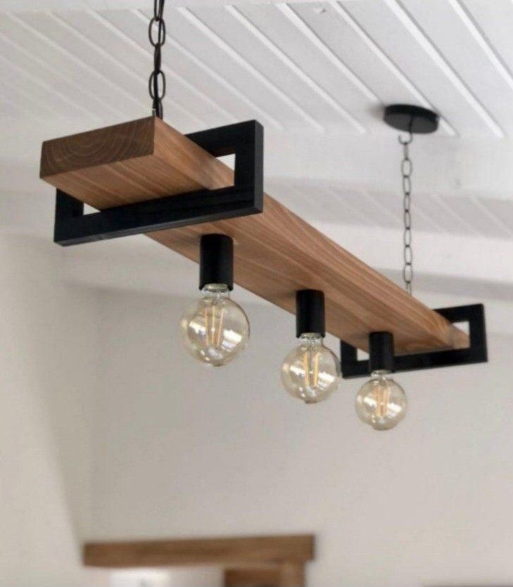 Lámpara colgante moderna de madera con tres bombillas expuestas y detalles en metal negro, suspendida del techo por cadenas. Diseño industrial elegante para interiores.