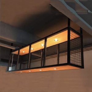 Lámpara colgante rectangular de diseño industrial con estructura de metal negro y paneles de rejilla. Cuenta con luces empotradas en su base interior de acabado madera cálida.