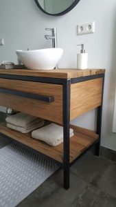 Mueble de baño moderno con estructura de metal negro y madera natural, lavabo blanco sobre encimera. Estante inferior con toallas beige, diseño minimalista y funcional.